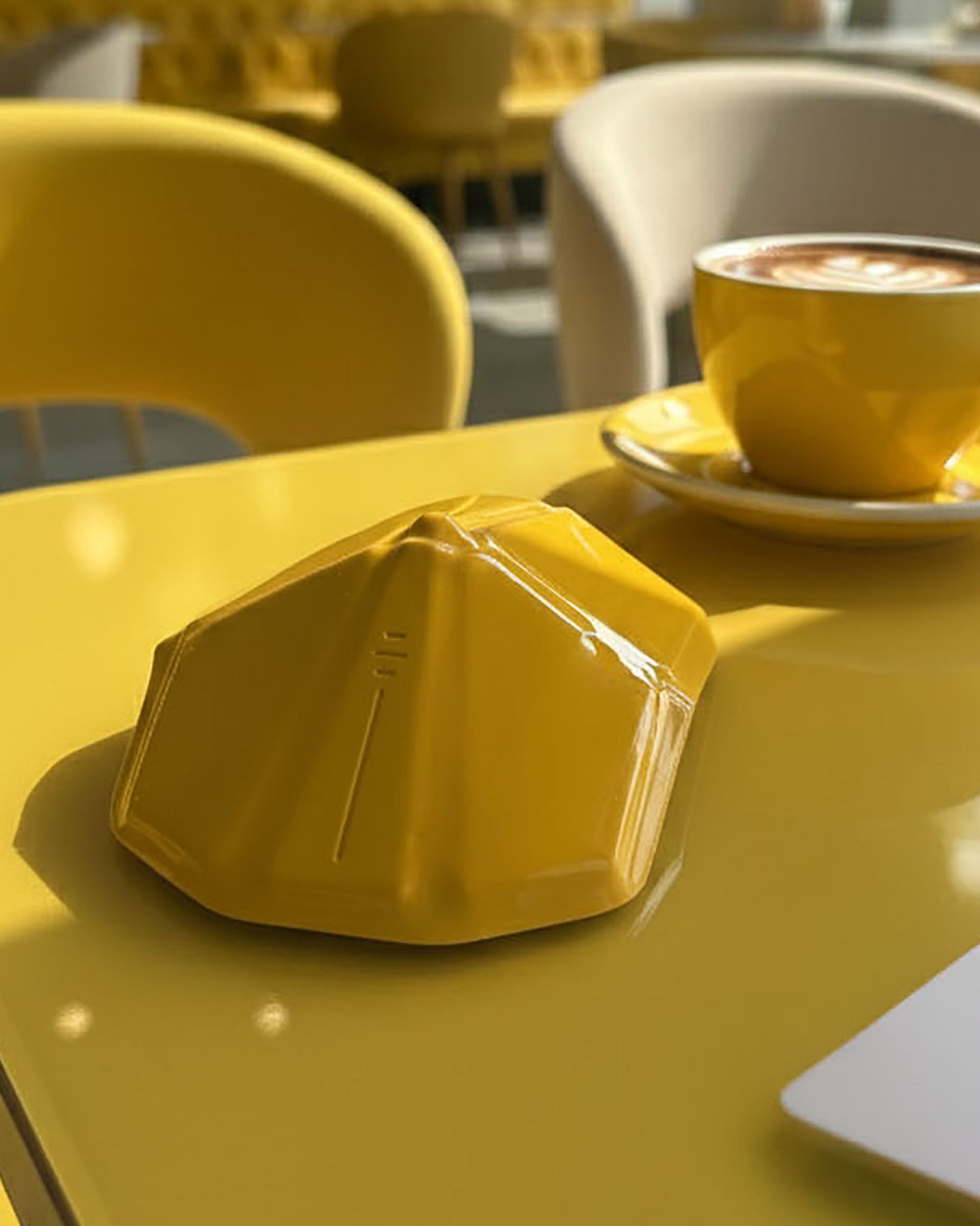 Yellow cupcake and yellow coffee cup on a yellow table with blurred chairs and tables in the background