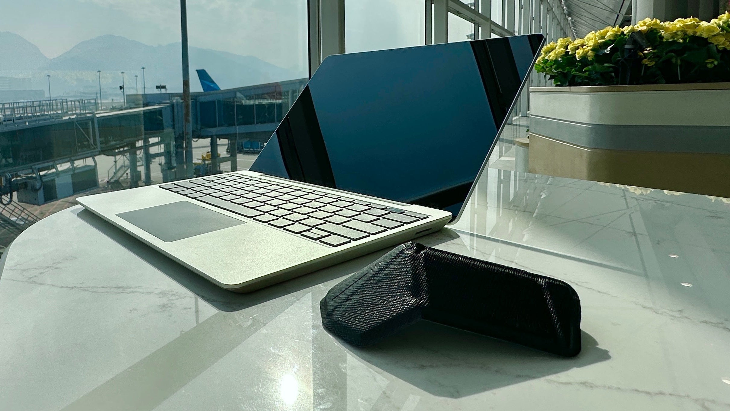 Laptop and smartphone on a table with airport view through large windows